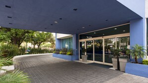 Un edificio moderno con fachada azul, zona de entrada con azulejos y plantas en macetas.