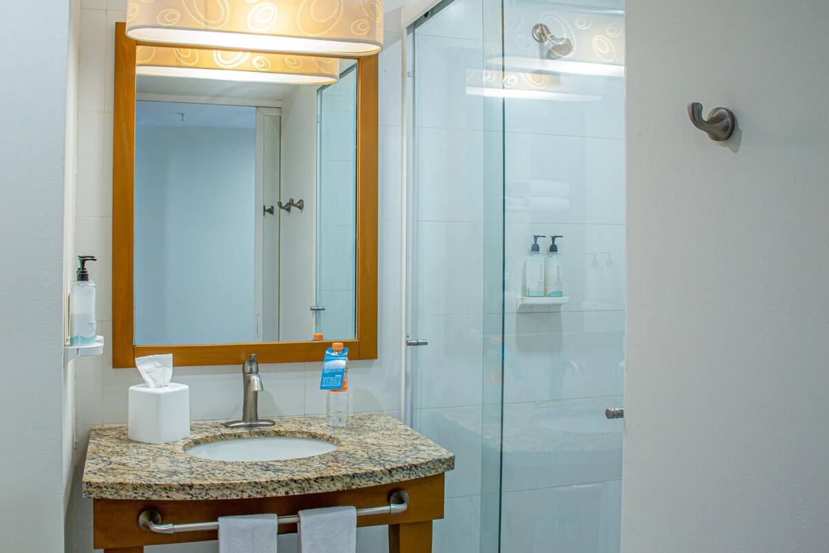 Un baño con lavamanos de granito, un espejo, toallero y cabina de ducha de vidrio.