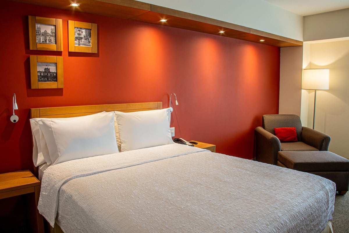 Una habitación de hotel con una cama grande, una silla, una mesita de noche y una lámpara.