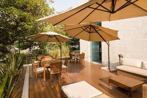 Eine Außenpatio mit Holztischen und -stühlen, beigen Sonnenschirmen und einem weißen Sofa.