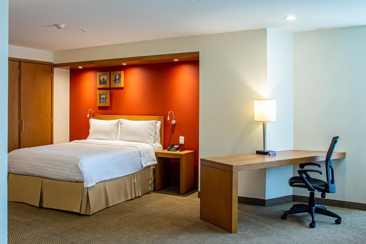 Una habitación de hotel con cama, escritorio, silla, mesita de noche y lámpara.
