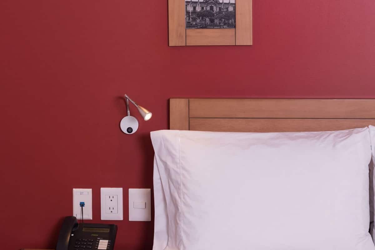 Habitación de hotel con cama, escritorio con teléfono, lámpara y tres cuadros en la pared.