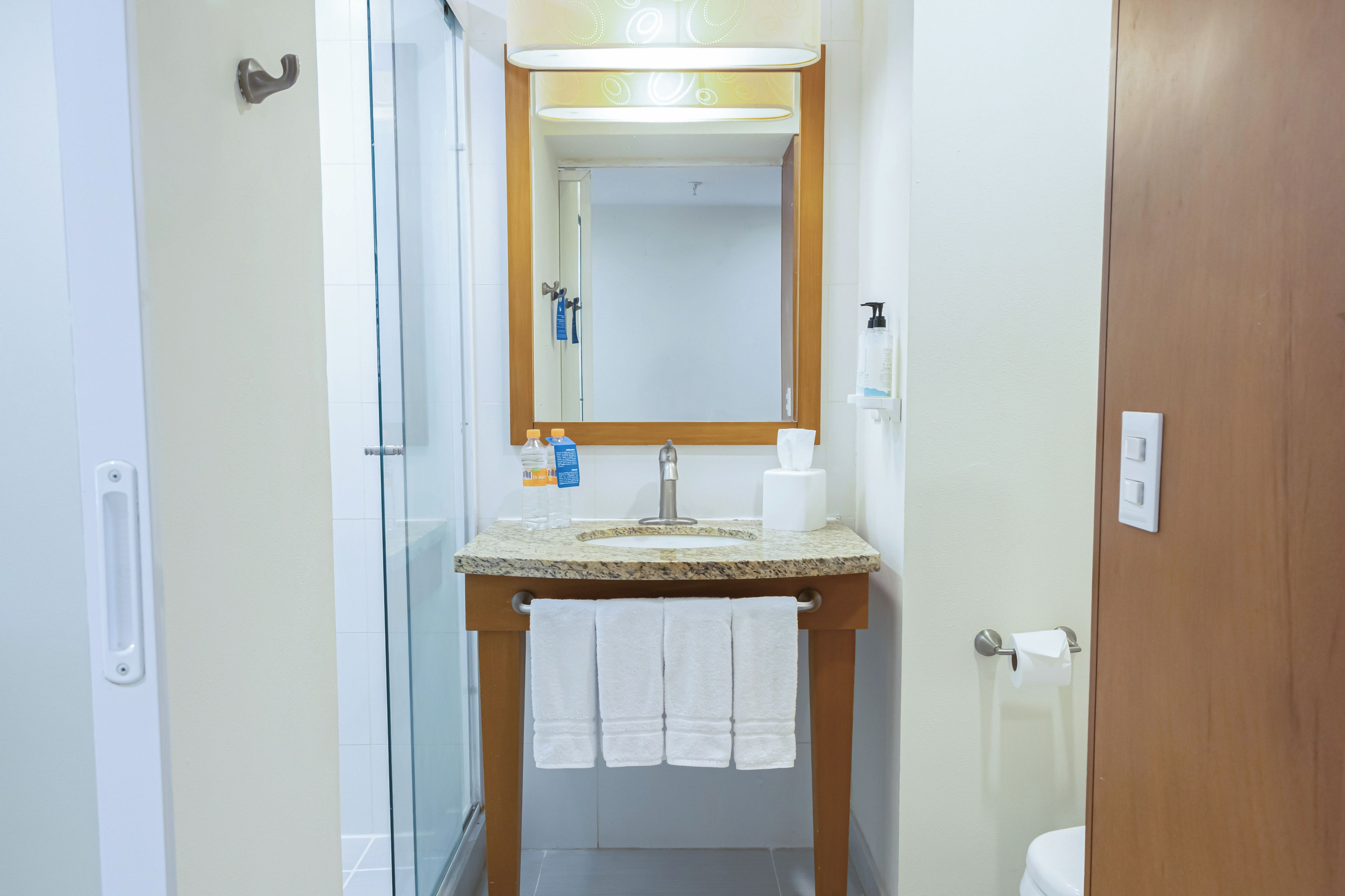 Un baño con cabina de ducha de vidrio, un lavabo con encimera de mármol, un espejo sobre el lavabo y una toalla colgada en la pared.