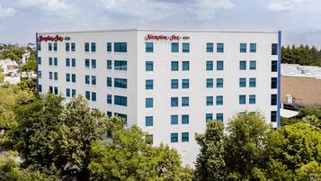 Um hotel Hampton Inn com vários andares, fachada branca e inúmeras janelas.
