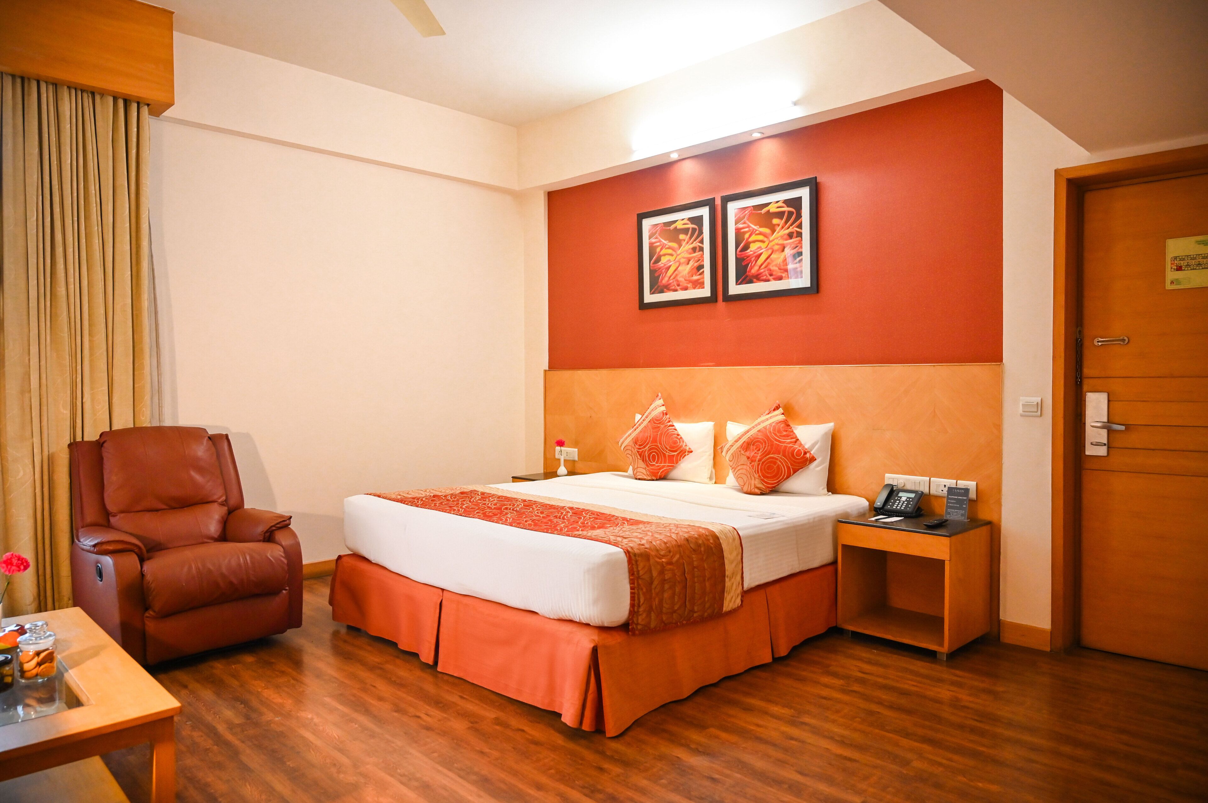 A hotel room with a bed, a chair, a bedside table with a phone, and a door.