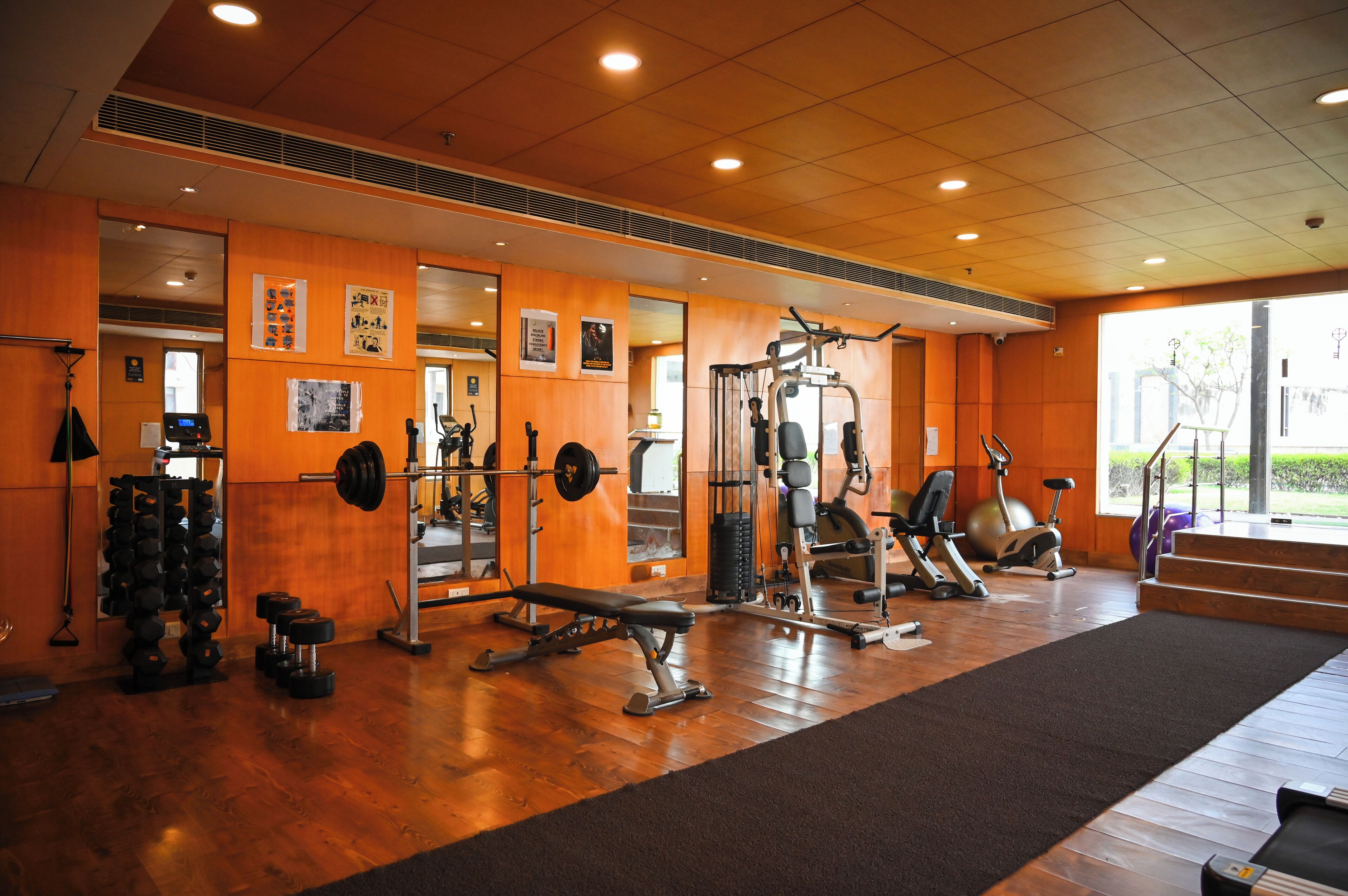 A gym with various exercise equipment, a mirror, and a window providing natural light.
