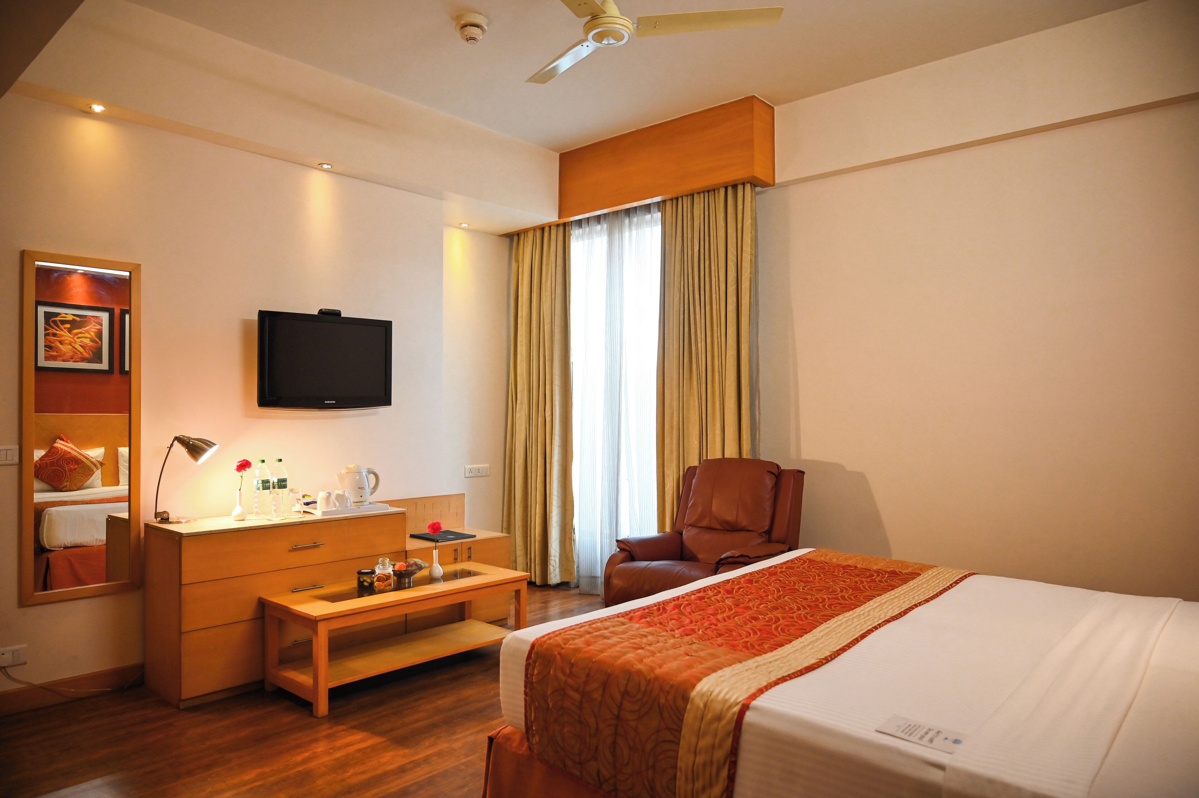A hotel room with a bed, a desk with a lamp, a chair, a television, and a window with curtains.