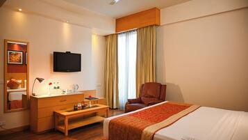 A hotel room with a bed, a desk with a lamp, a chair, a television, and a window with curtains.