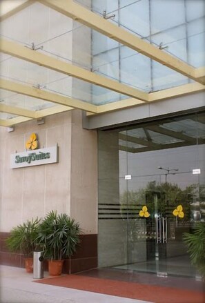 L’entrée d’un hôtel avec une façade en verre, une enseigne indiquant « Sunny Suites », et des plantes en pot à l’extérieur.