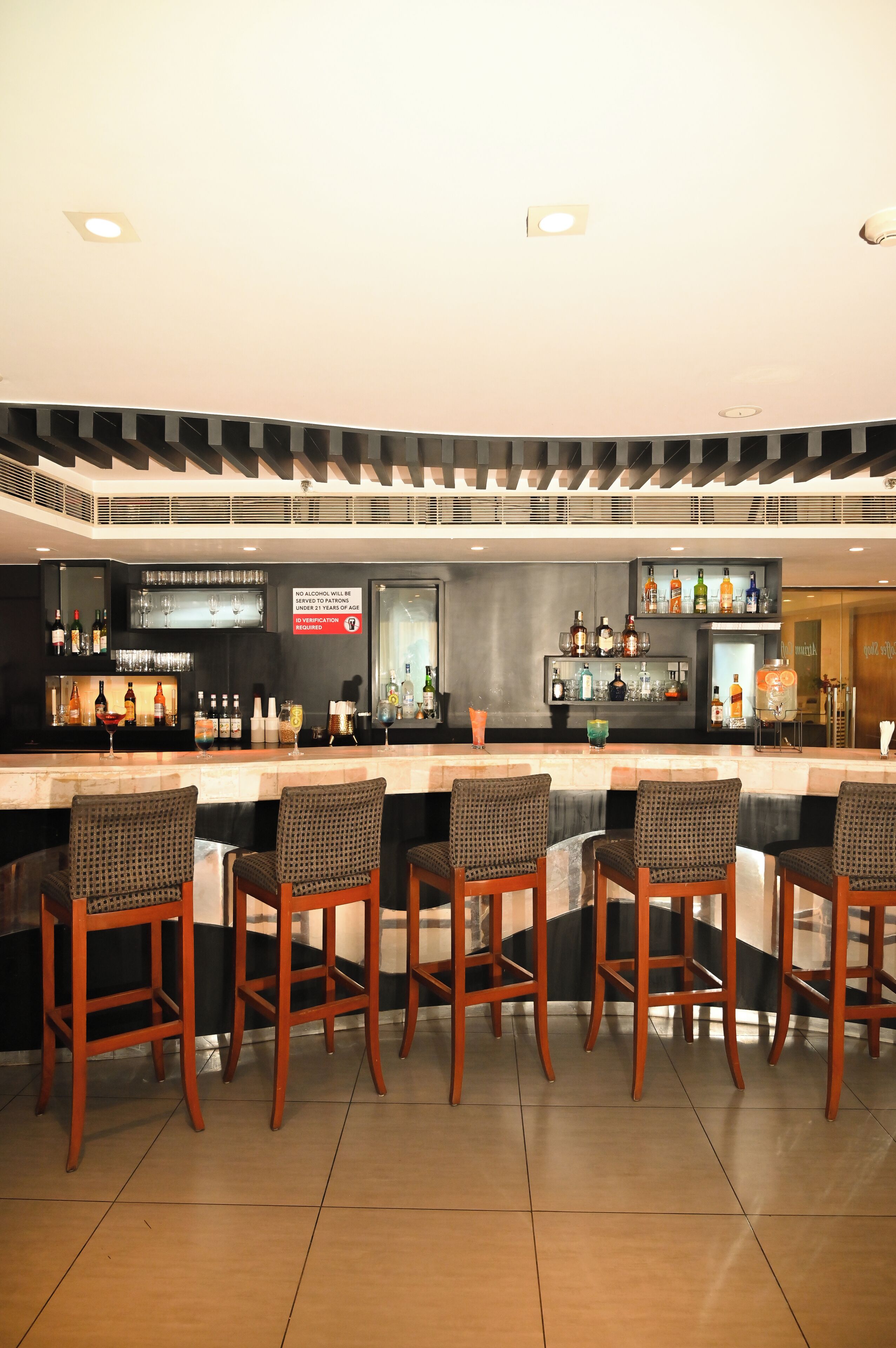 Zona de bar con mostrador, varios taburetes y una variedad de botellas y vasos.