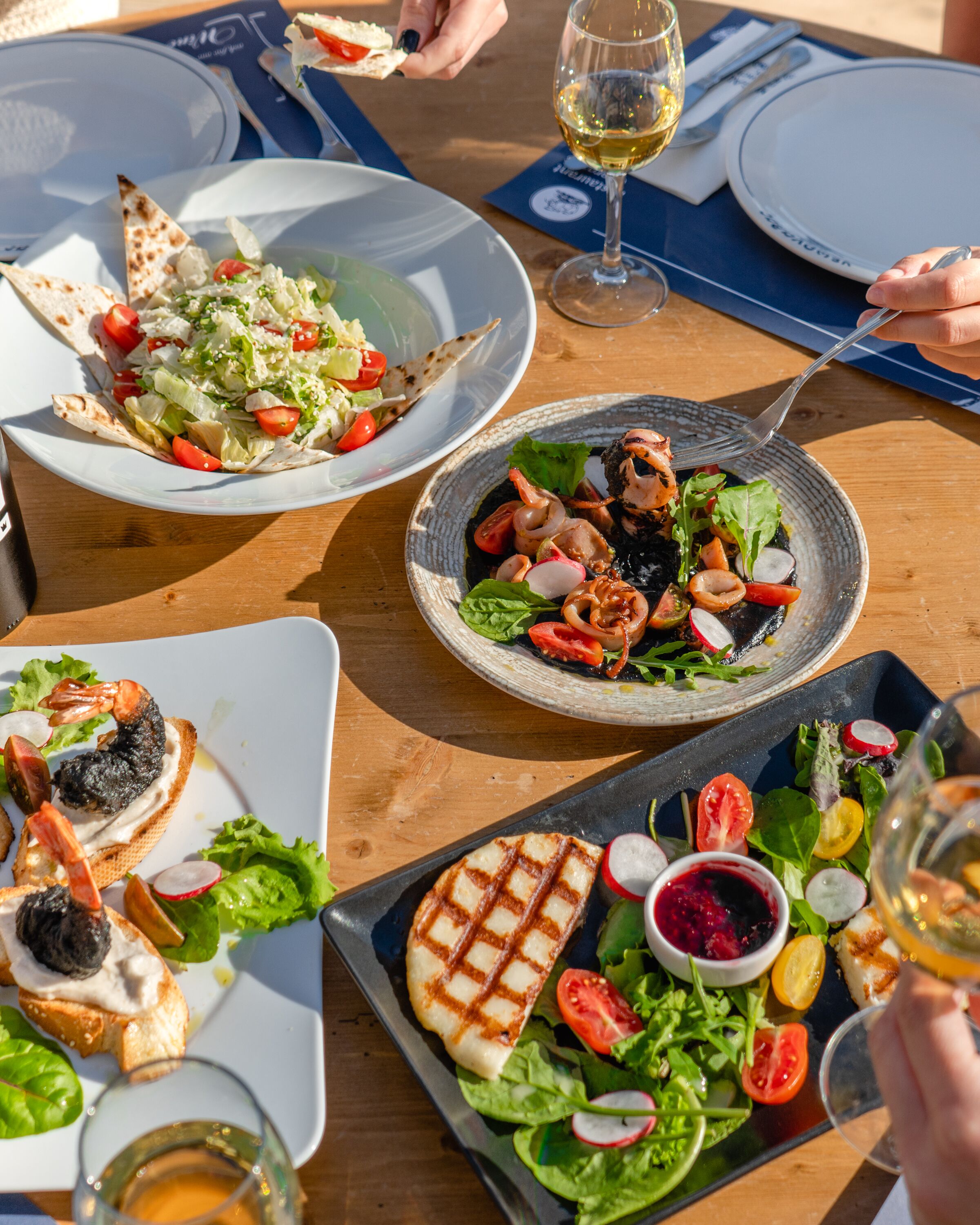 Una mesa con diferentes platos, entre ellos ensaladas, preparaciones a la parrilla y mariscos, lo que sugiere un ambiente de comedor.
