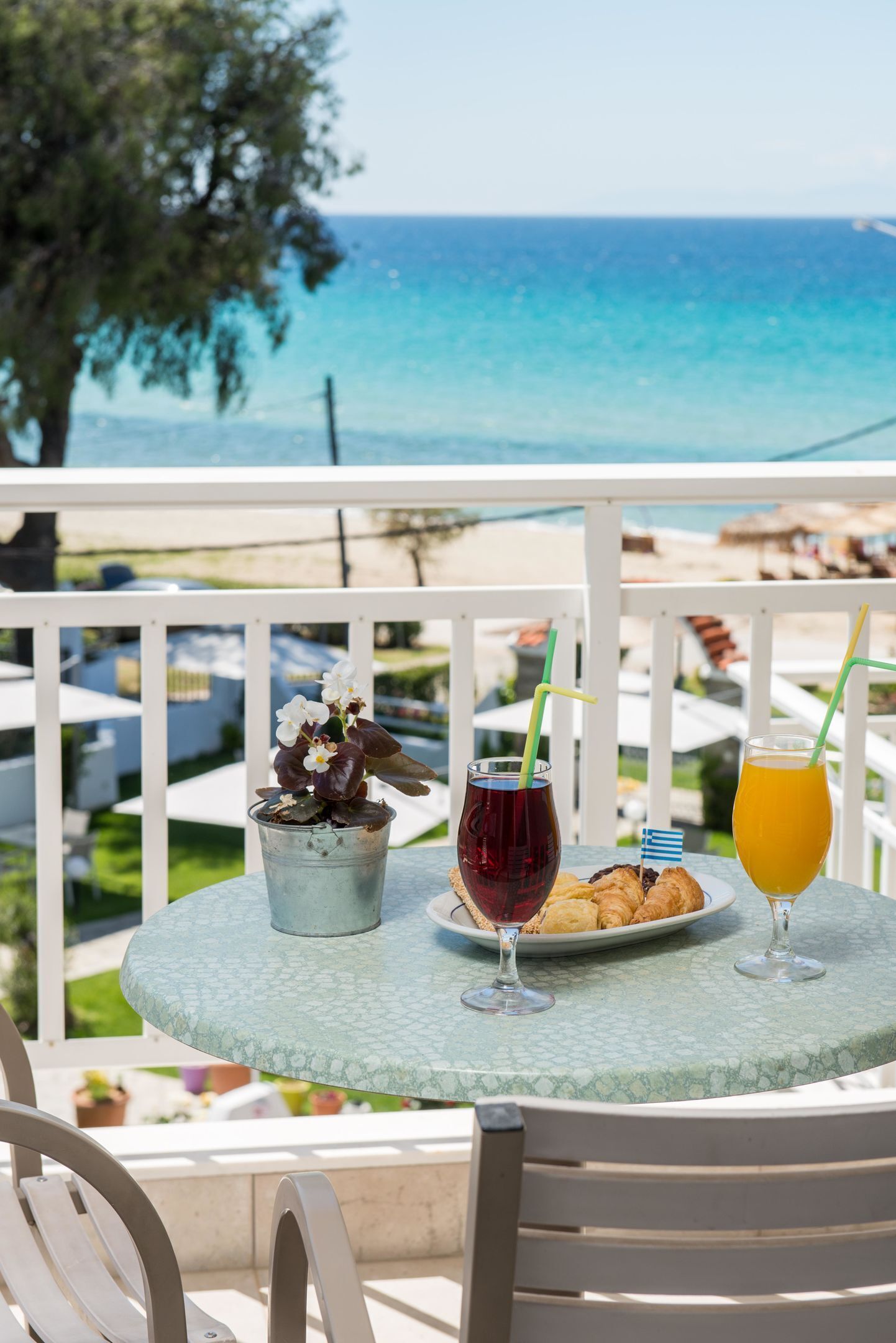 A table with drinks and pastries on a balcony overlooking the sea.