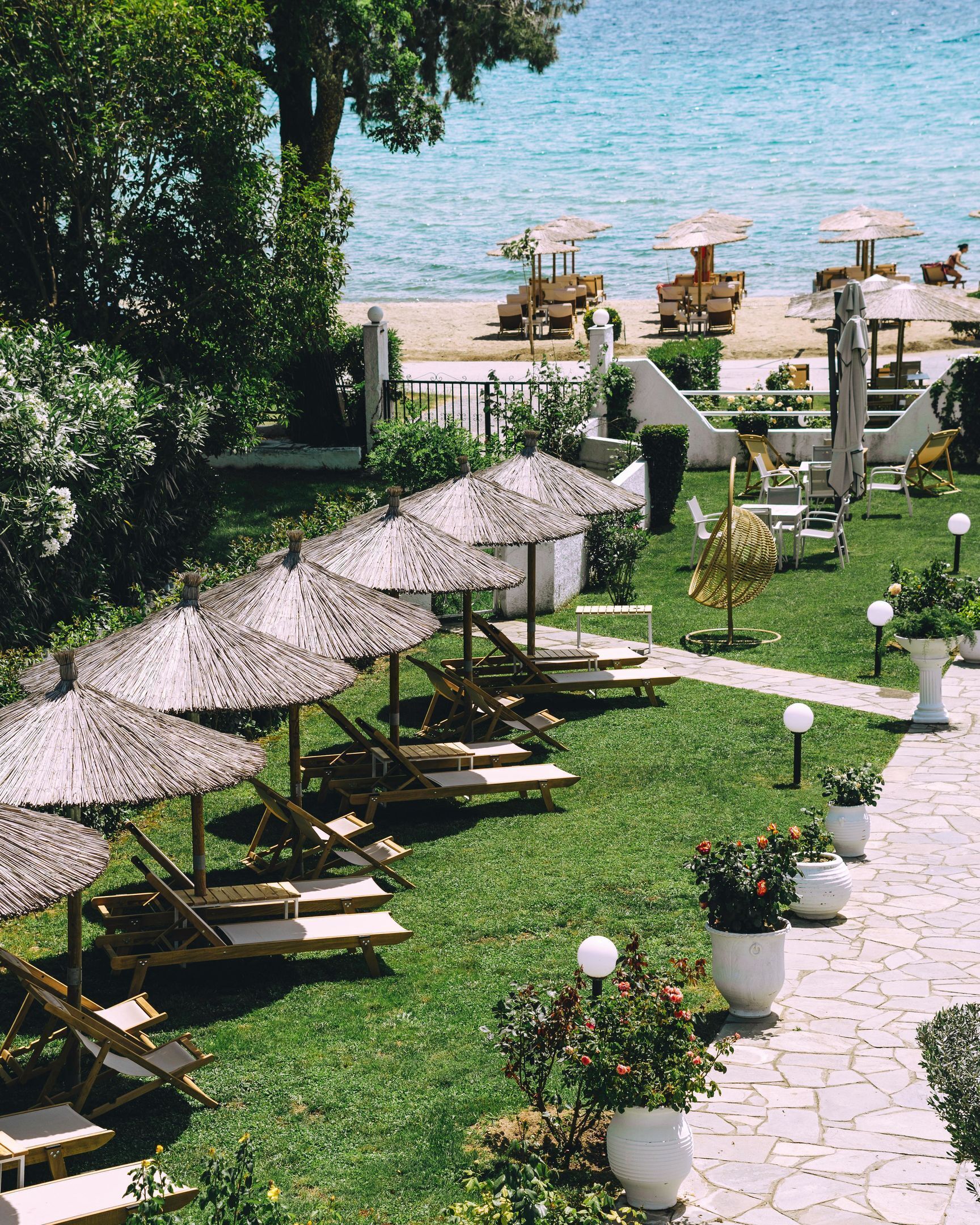 A resort with outdoor seating areas, including wooden lounge chairs and thatched umbrellas, arranged on a well-maintained lawn with potted plants.