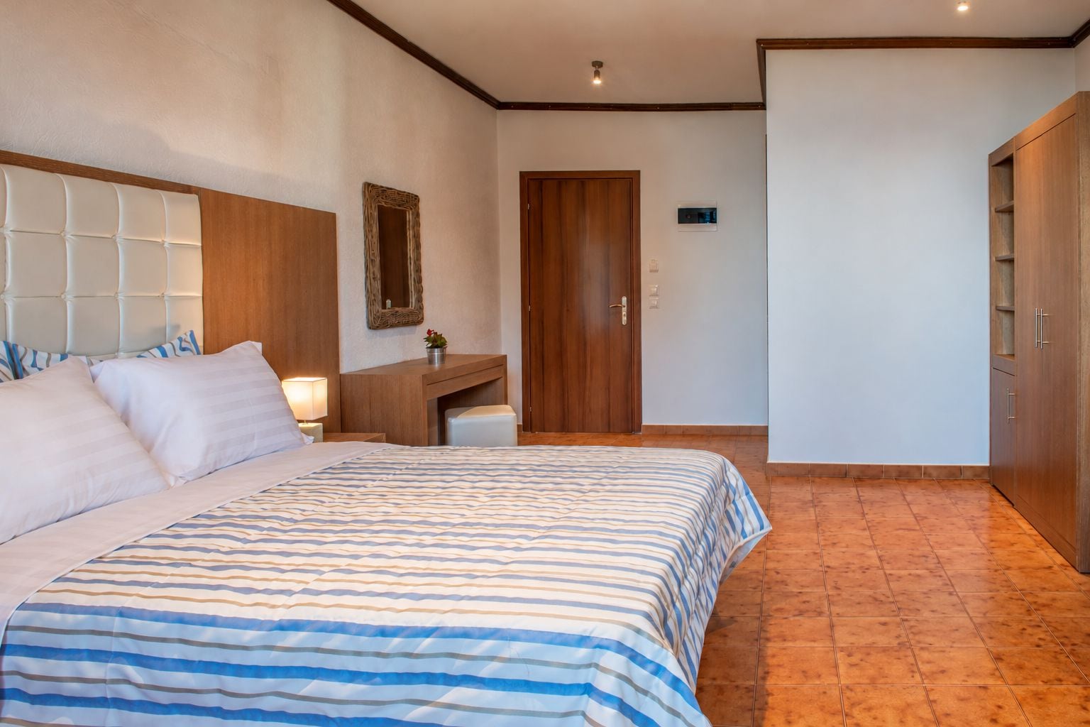 Ein Hotelzimmer mit einem großen Bett, einem Holztisch, einem Schrank und einer Tür.