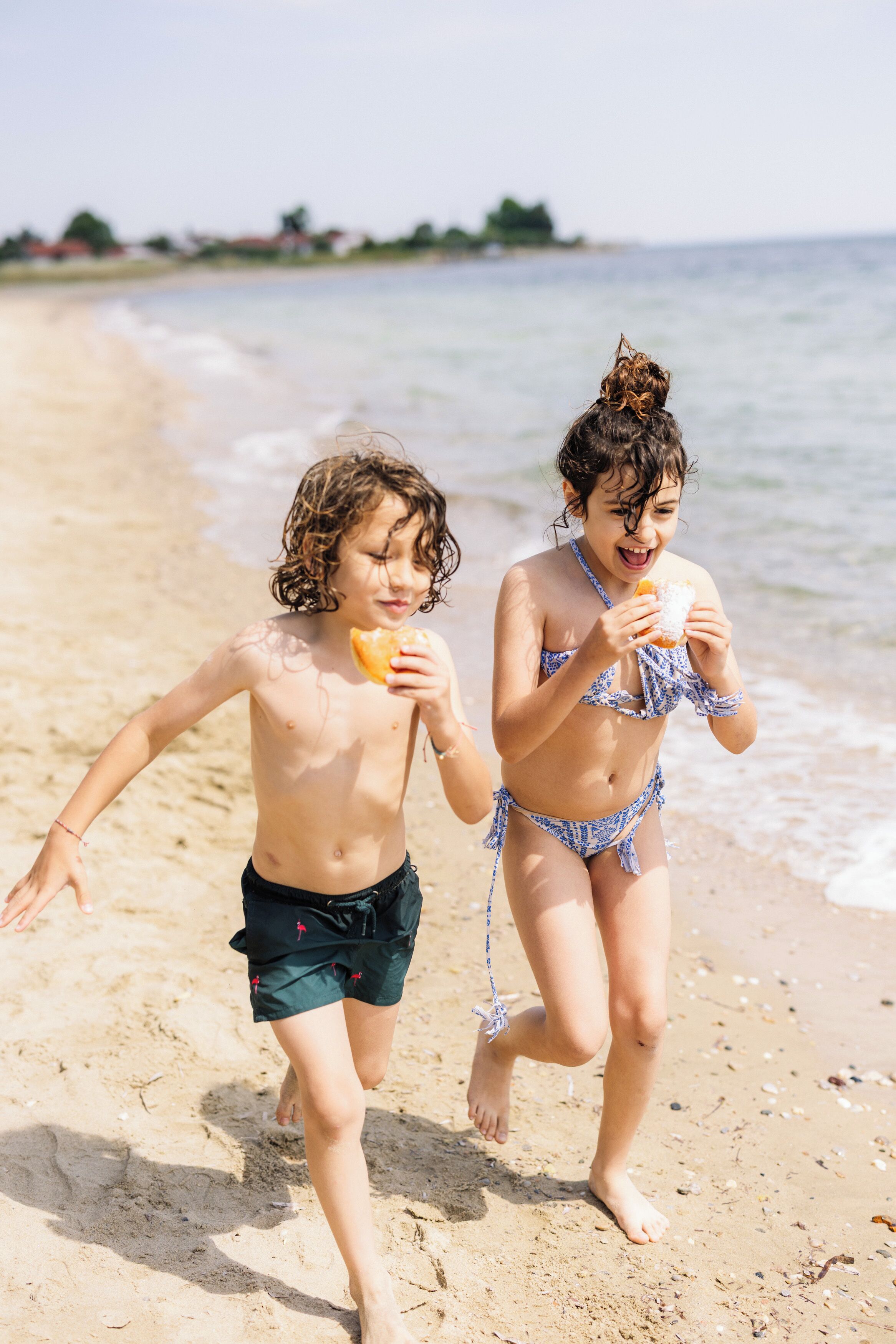 Dos niños corriendo en una playa arenosa con el océano al fondo.