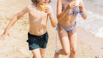 Dos niños corriendo en una playa arenosa con el océano al fondo.