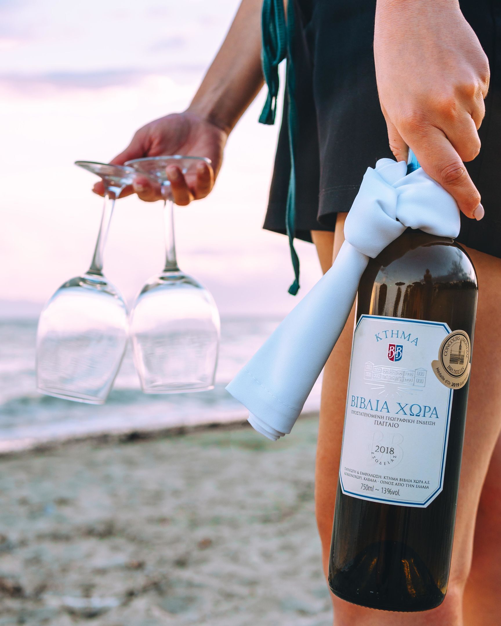 Una persona sosteniendo una botella de vino con etiqueta y dos copas de vino vacías.