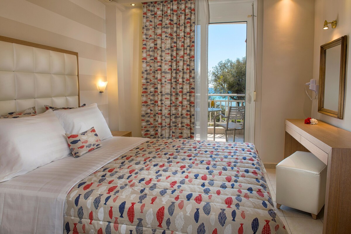 A bedroom with a bed, a bedside table, a mirror, and a view of the outdoors.