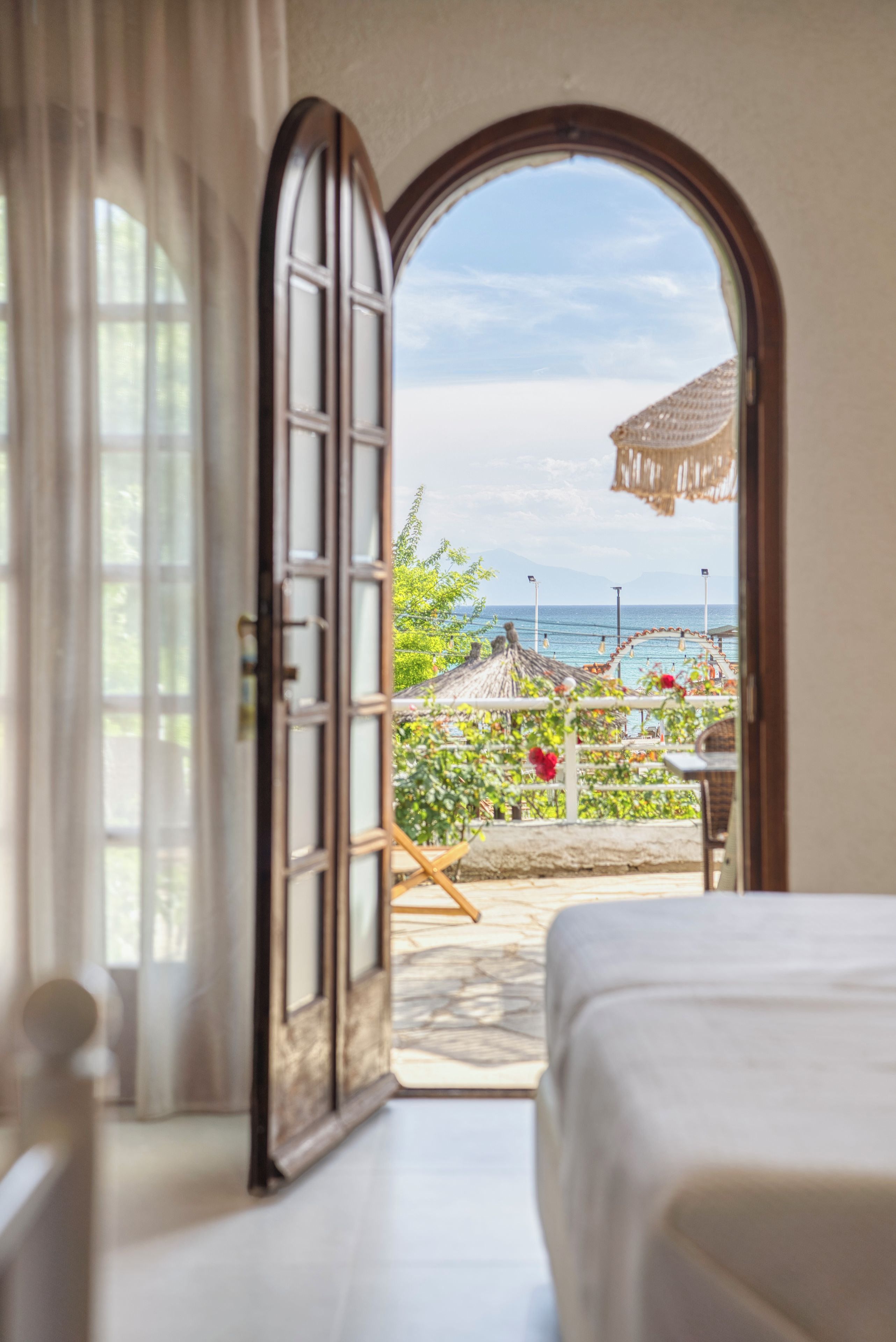 Une chambre avec un lit, une porte ouverte donnant sur un balcon avec vue sur la mer et un parasol en chaume.
