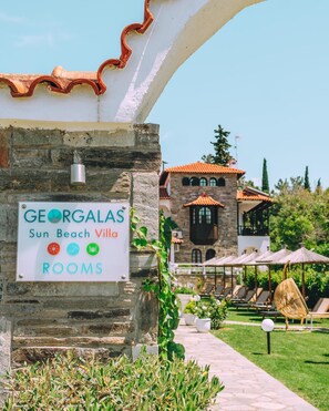 A sign for Georgalas Sun Beach Villa with a stone wall and a view of the villa's exterior. - Georgalas Sun Beach Resort (Nea Propontida)