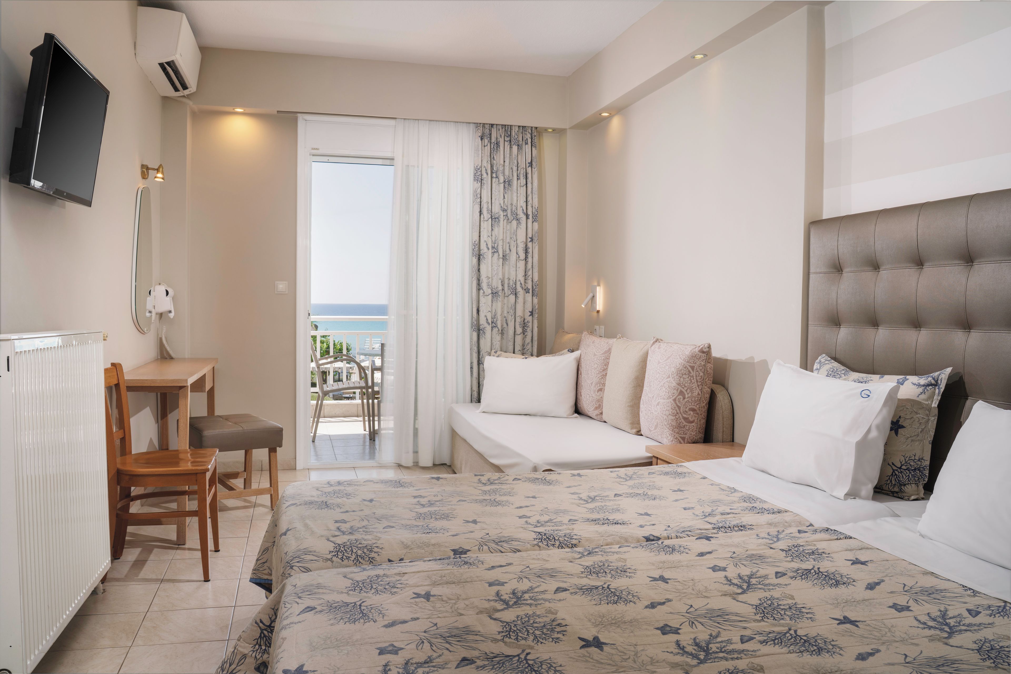 Una habitación de hotel con cama, escritorio, silla, balcón con vistas y televisor montado en la pared.