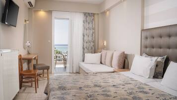 Una habitación de hotel con cama, escritorio, silla, balcón con vistas y televisor montado en la pared.