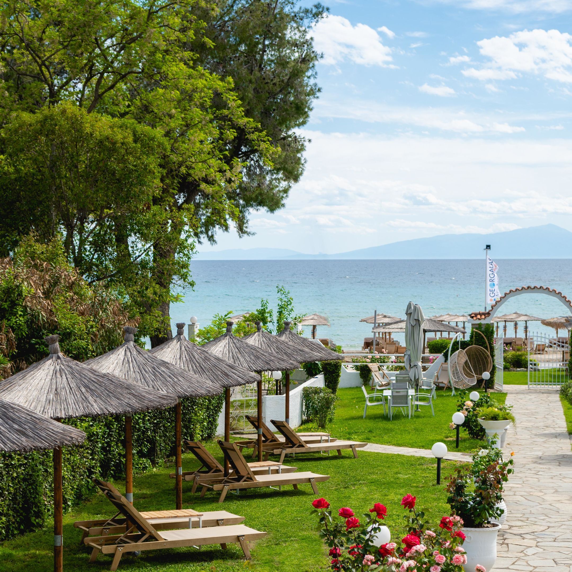Un complejo turístico frente al mar con sillones de madera, sombrillas de paja y vistas al océano.