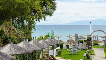 Un complejo turístico frente al mar con sillones de madera, sombrillas de paja y vistas al océano.
