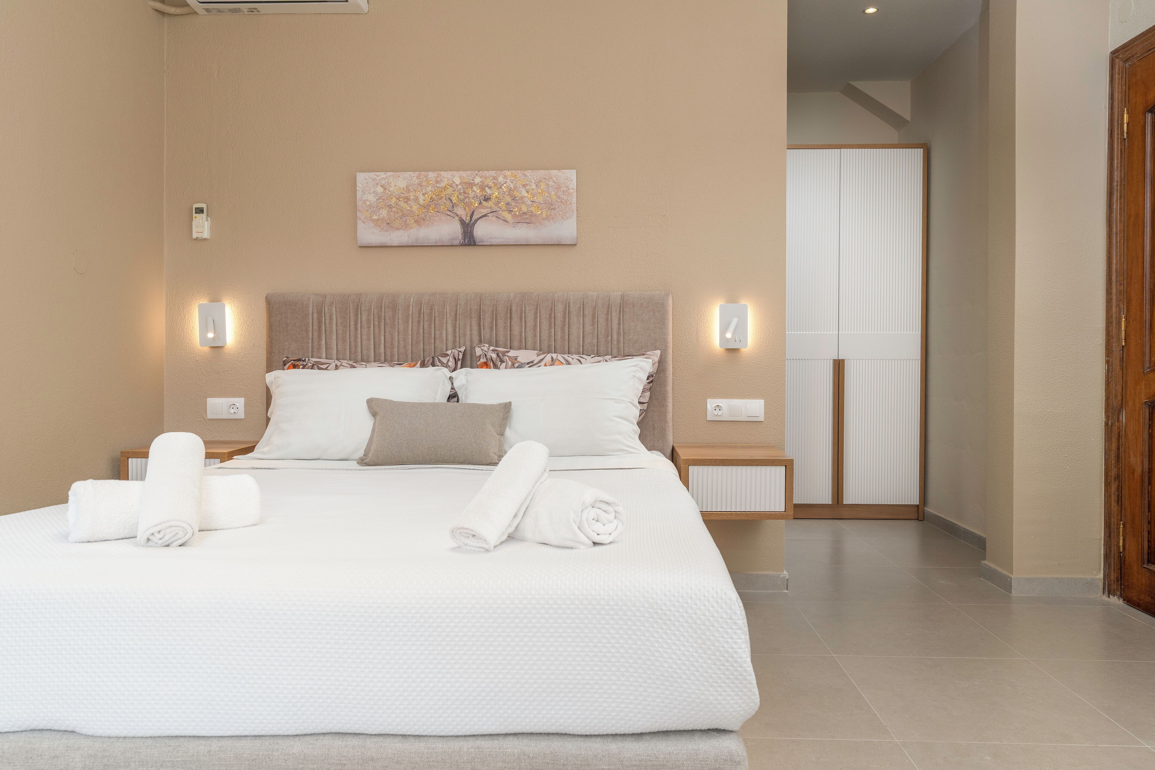 A spacious bedroom with a large bed, a headboard, two bedside tables, and a wall-mounted painting.