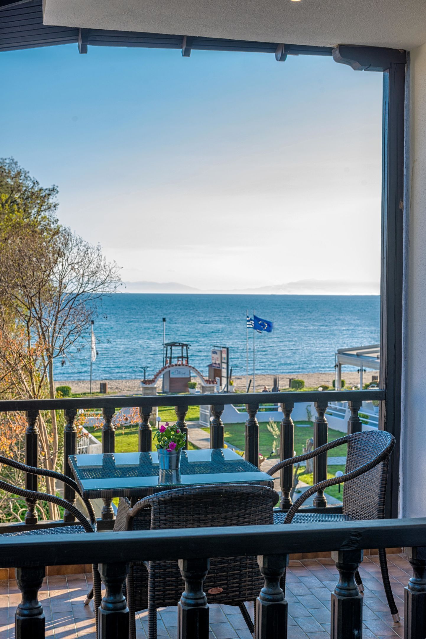Un balcon agrémenté de meubles en osier, d’une table en verre et offrant une vue sur la mer.