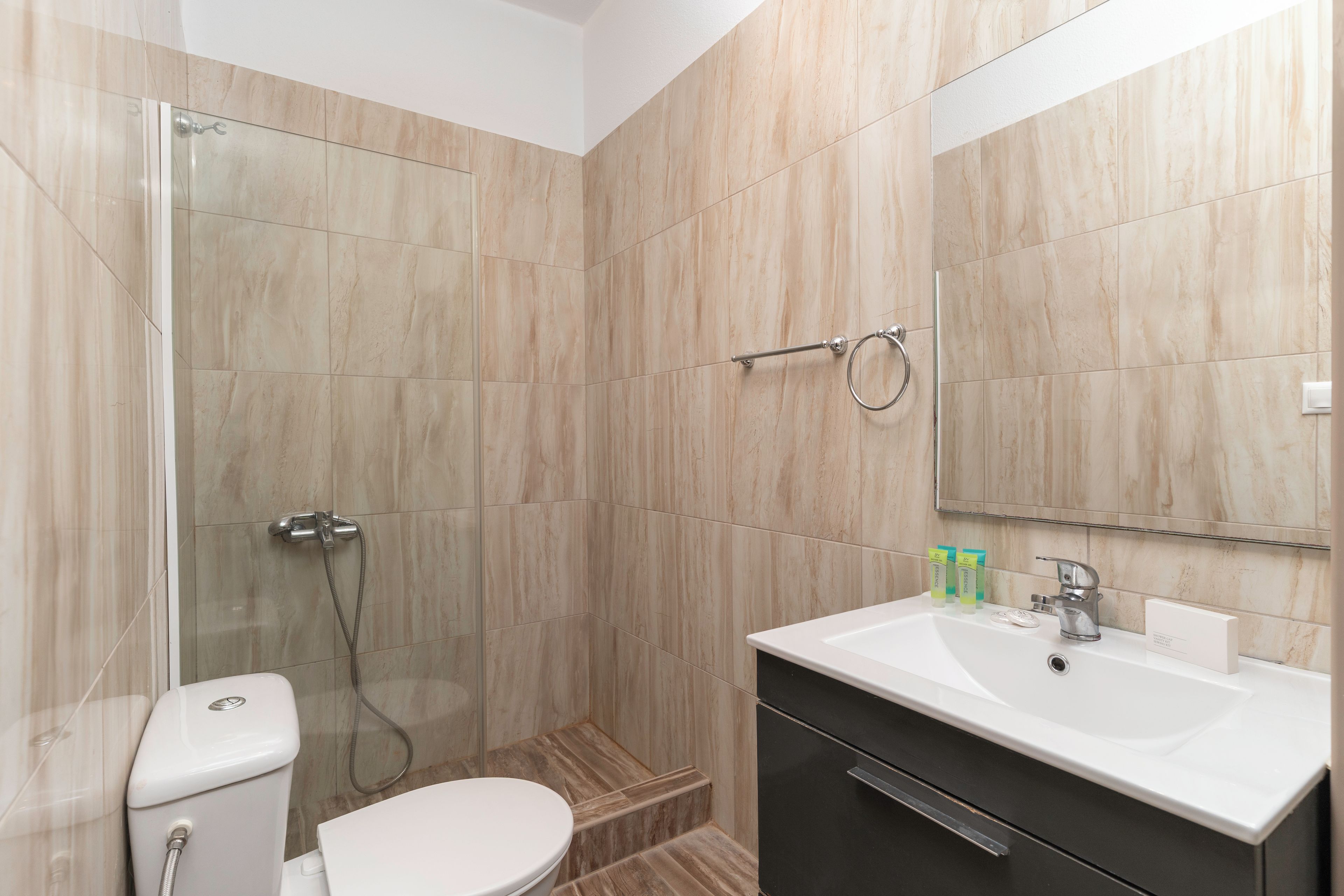 Une salle de bain moderne avec une douche à parois de verre, des toilettes blanches, un lavabo avec un miroir et un meuble sombre.