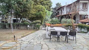 An outdoor patio with stone flooring, a table with chairs, and a garden with trees and shrubs.