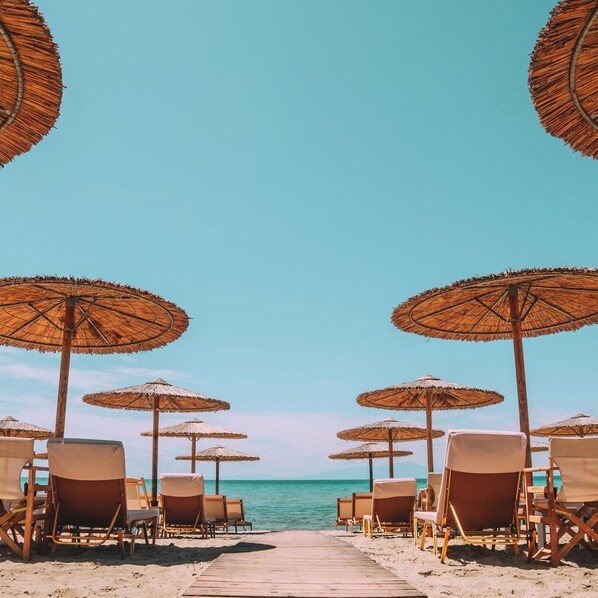 A beach with rows of sun loungers and thatched umbrellas, leading to the sea. - Georgalas Sun Beach Resort (Nea Propontida)