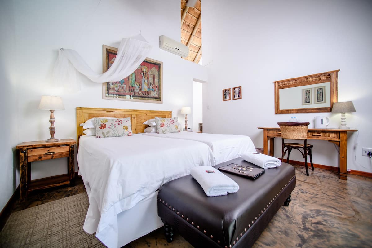 A hotel room with two beds, a desk, a chair, and a large mirror.