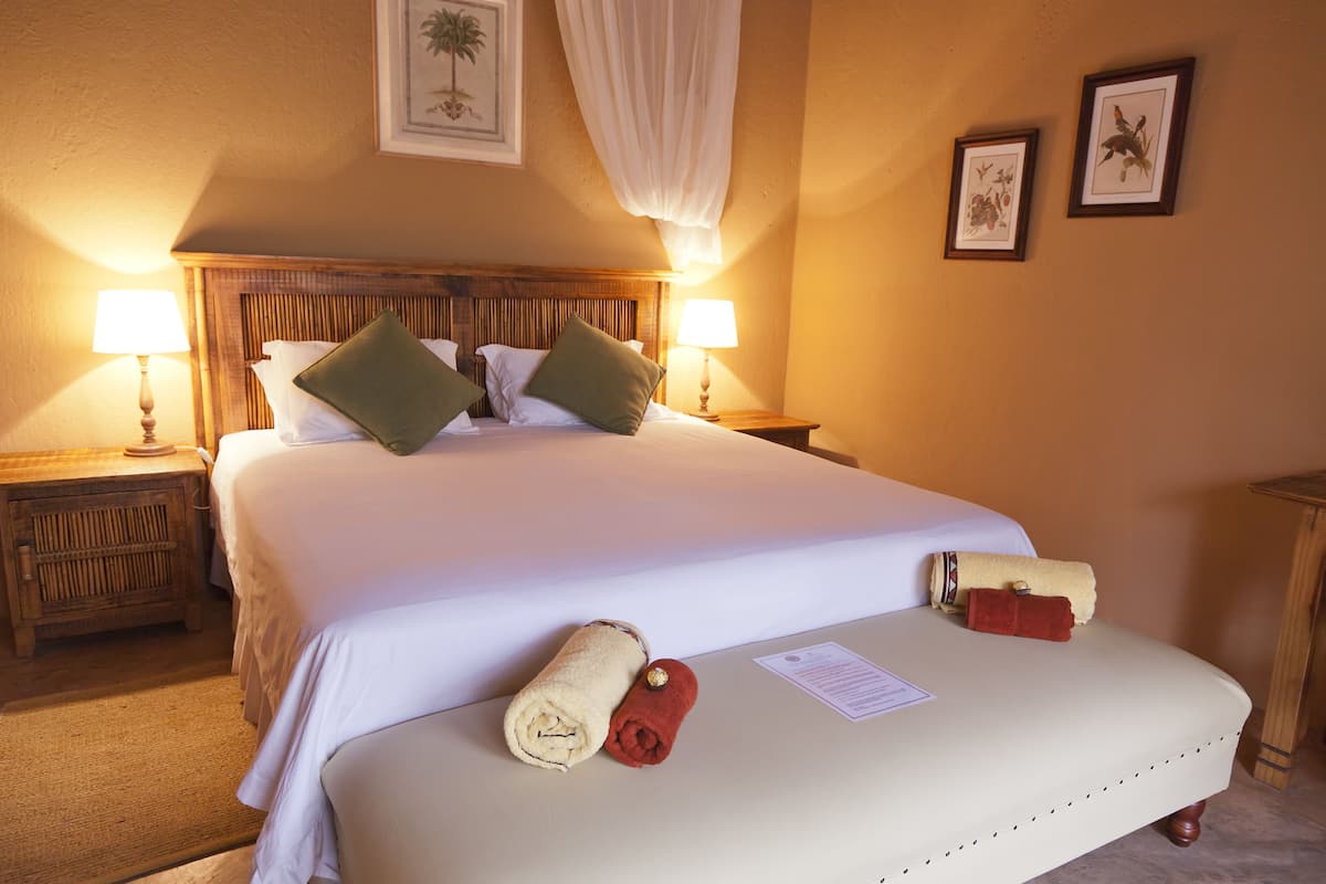 A neatly made bed with white linens, two pillows, and two rolled towels on the bed. There are two bedside lamps on wooden nightstands.