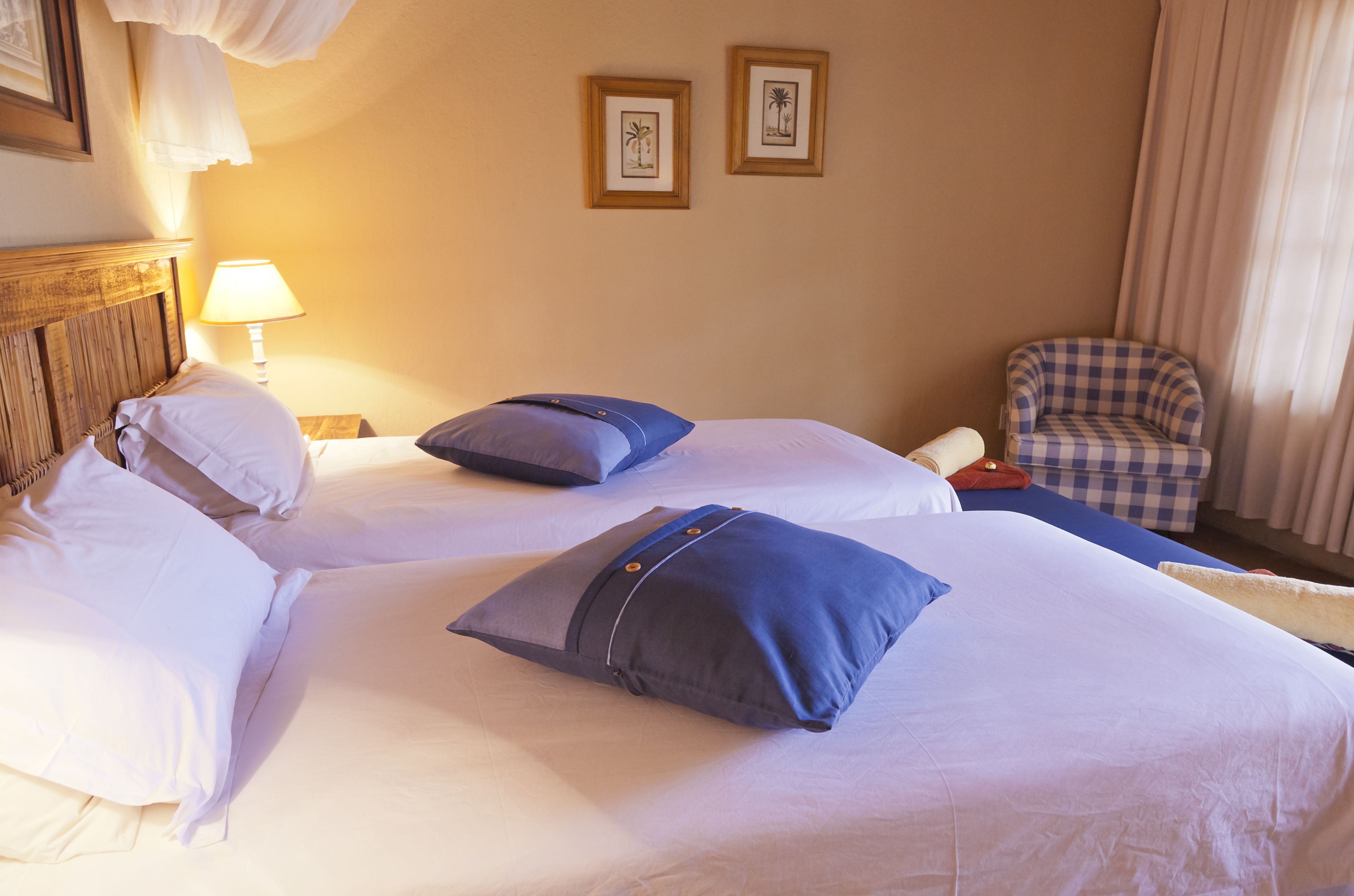Una habitación de hotel con dos camas, un sillón a cuadros y cuadros enmarcados en la pared.