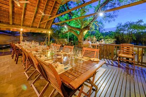 Enjoy a shaded meal under a thatched roof, surrounded by lush greenery and trees.