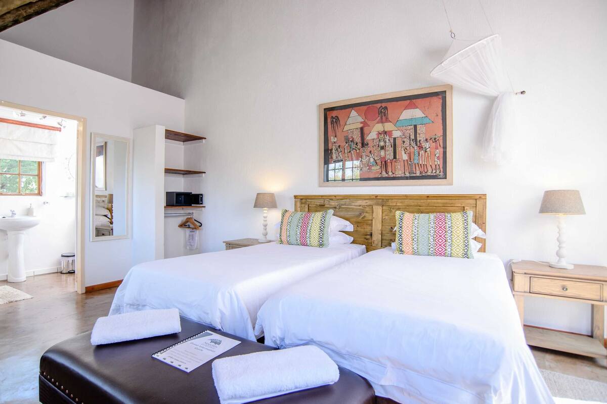 A hotel room with two beds, a wooden headboard, a painting on the wall, and a mosquito net.