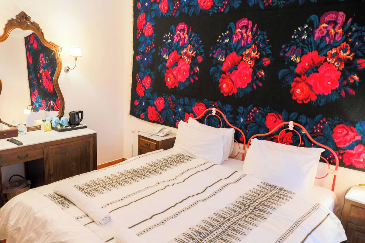 Ein ordentlich bezogenes Bett mit weißen Leinen und einer floralen Wandweberei dahinter.