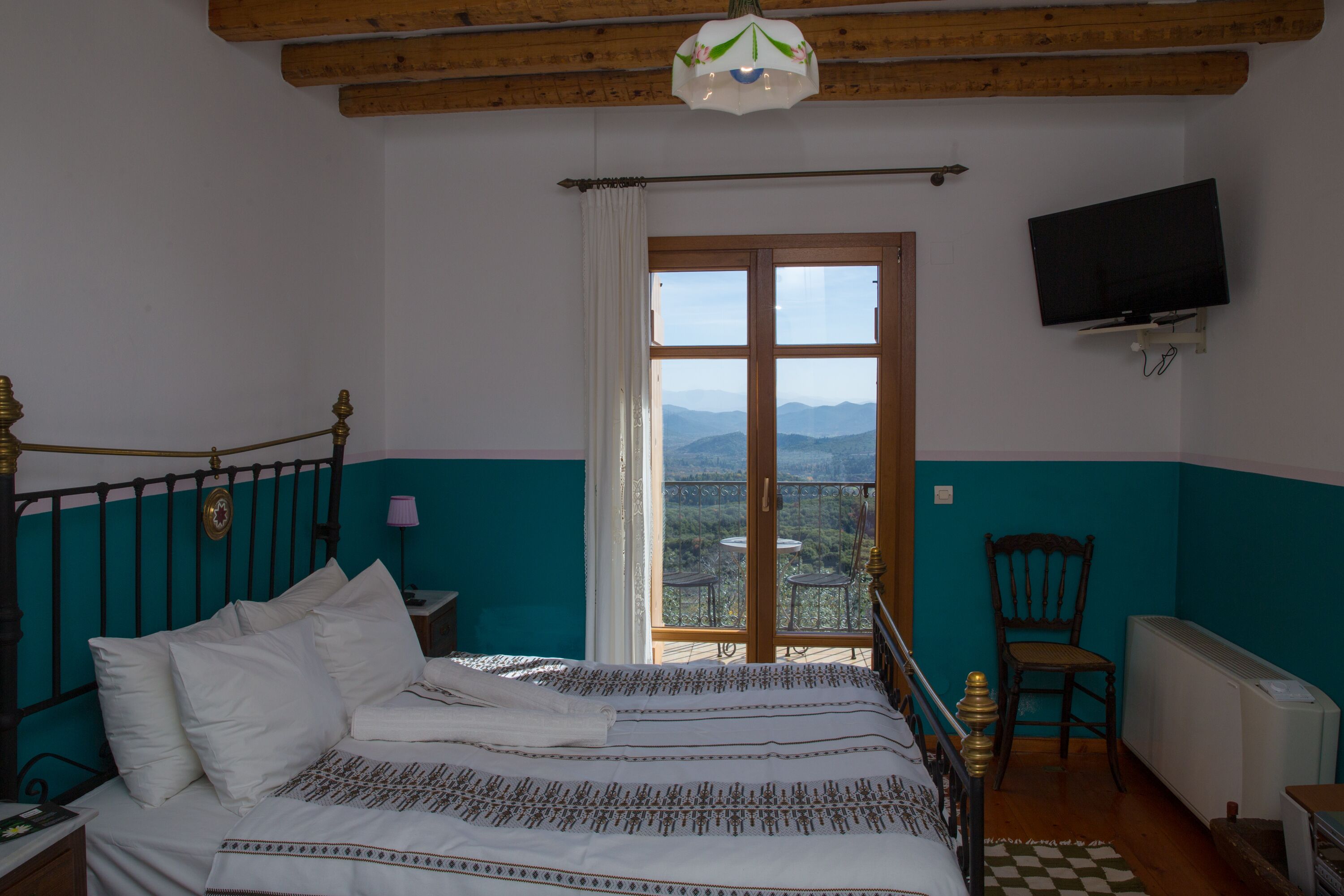 A bedroom with a bed, a TV mounted on the wall, a chair, and a view of the mountains through the window.