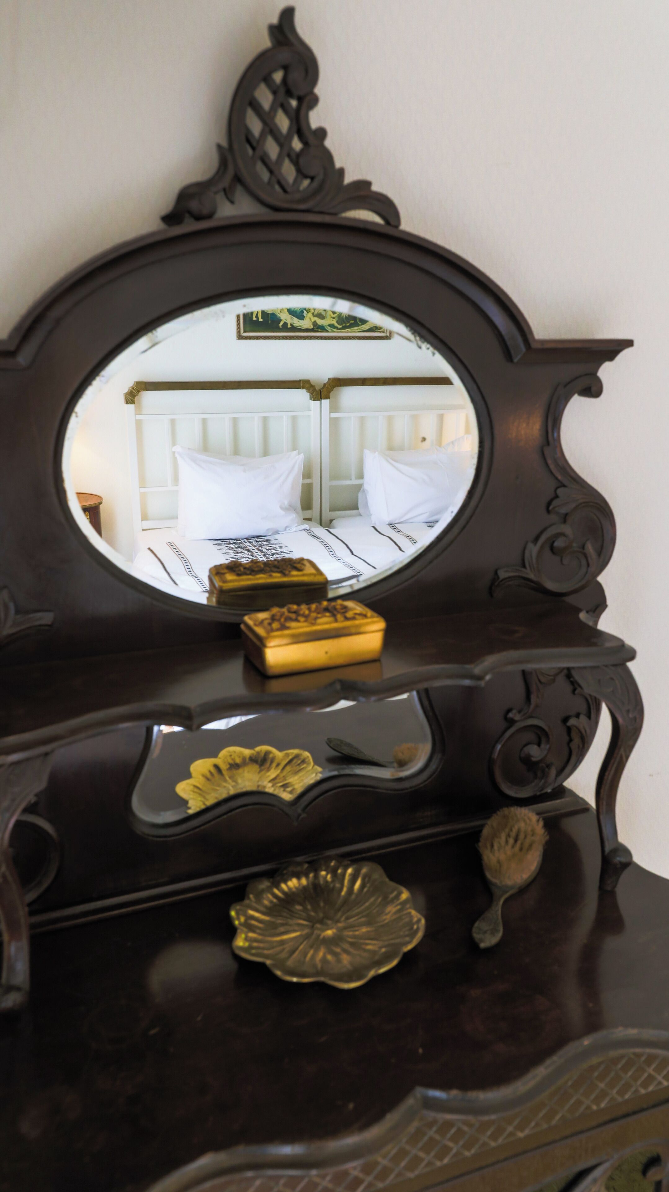 A dark wooden dresser with a mirror, a bed with white bedding, and decorative items including a small golden box and a flower-shaped object.