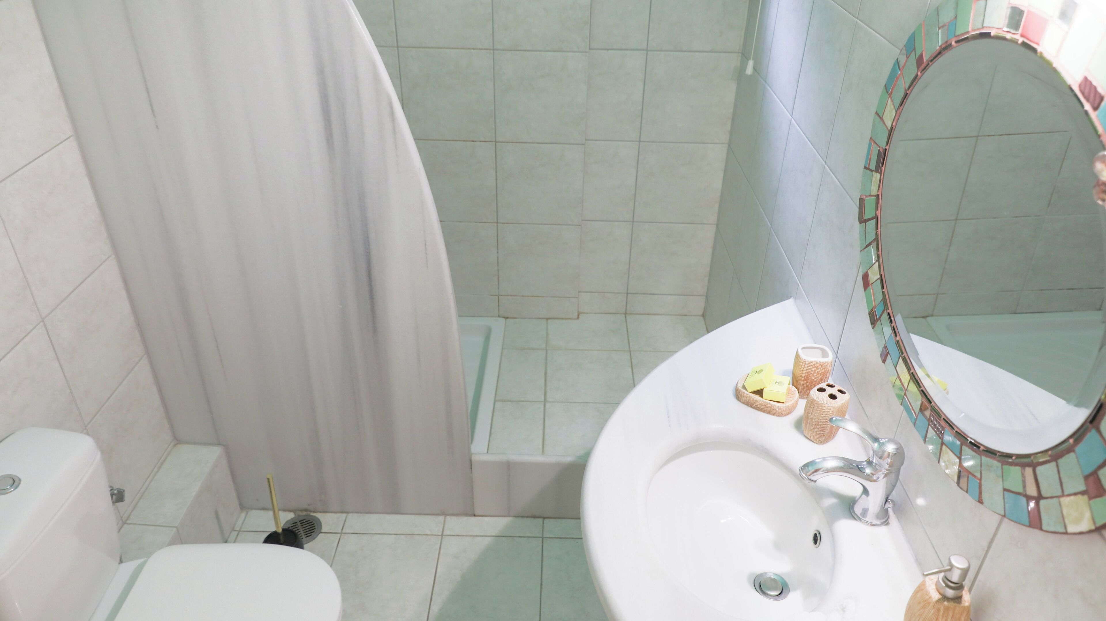 A bathroom with a shower, toilet, sink, and a mirror with a mosaic frame.