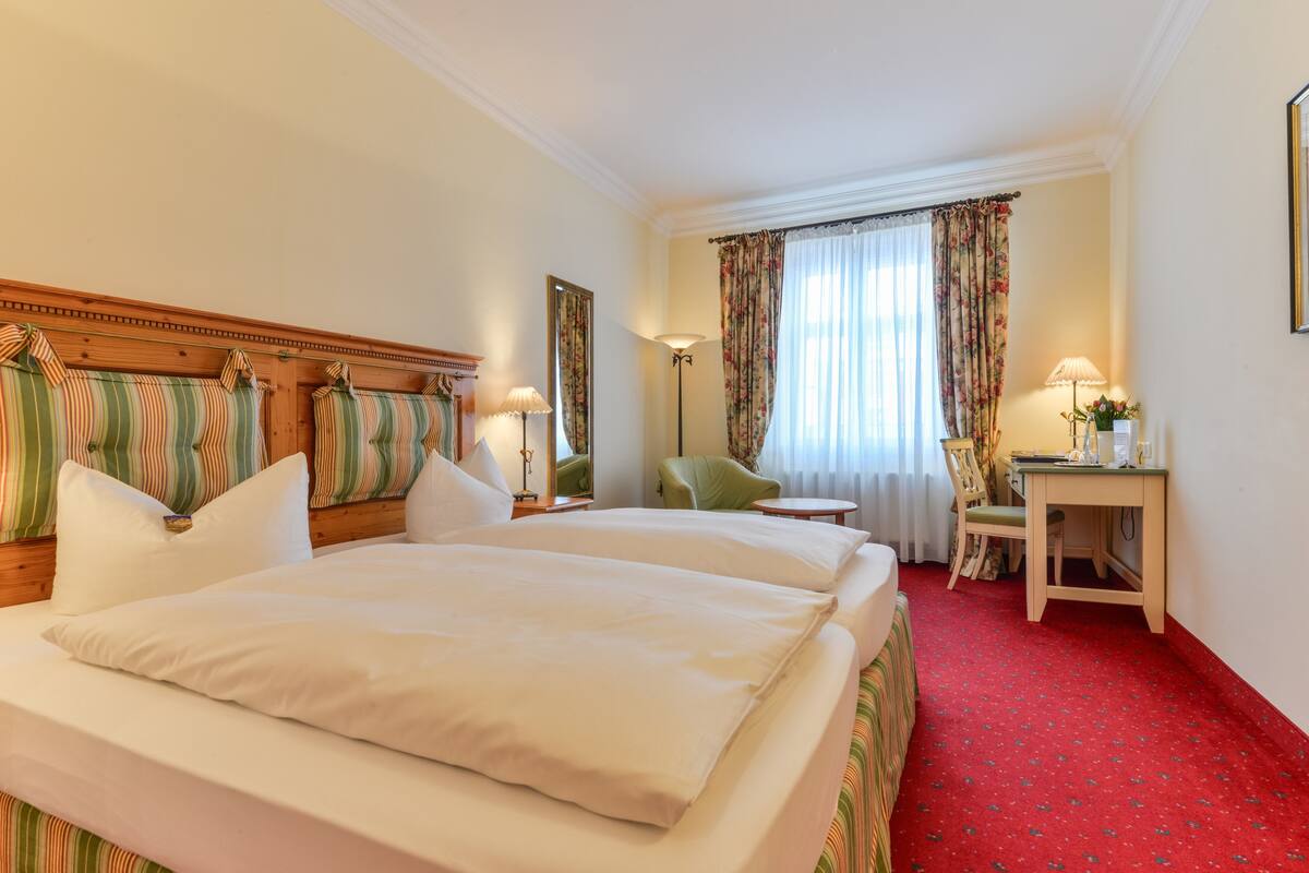 Una habitación de hotel con dos camas, un escritorio, una silla y una lámpara.