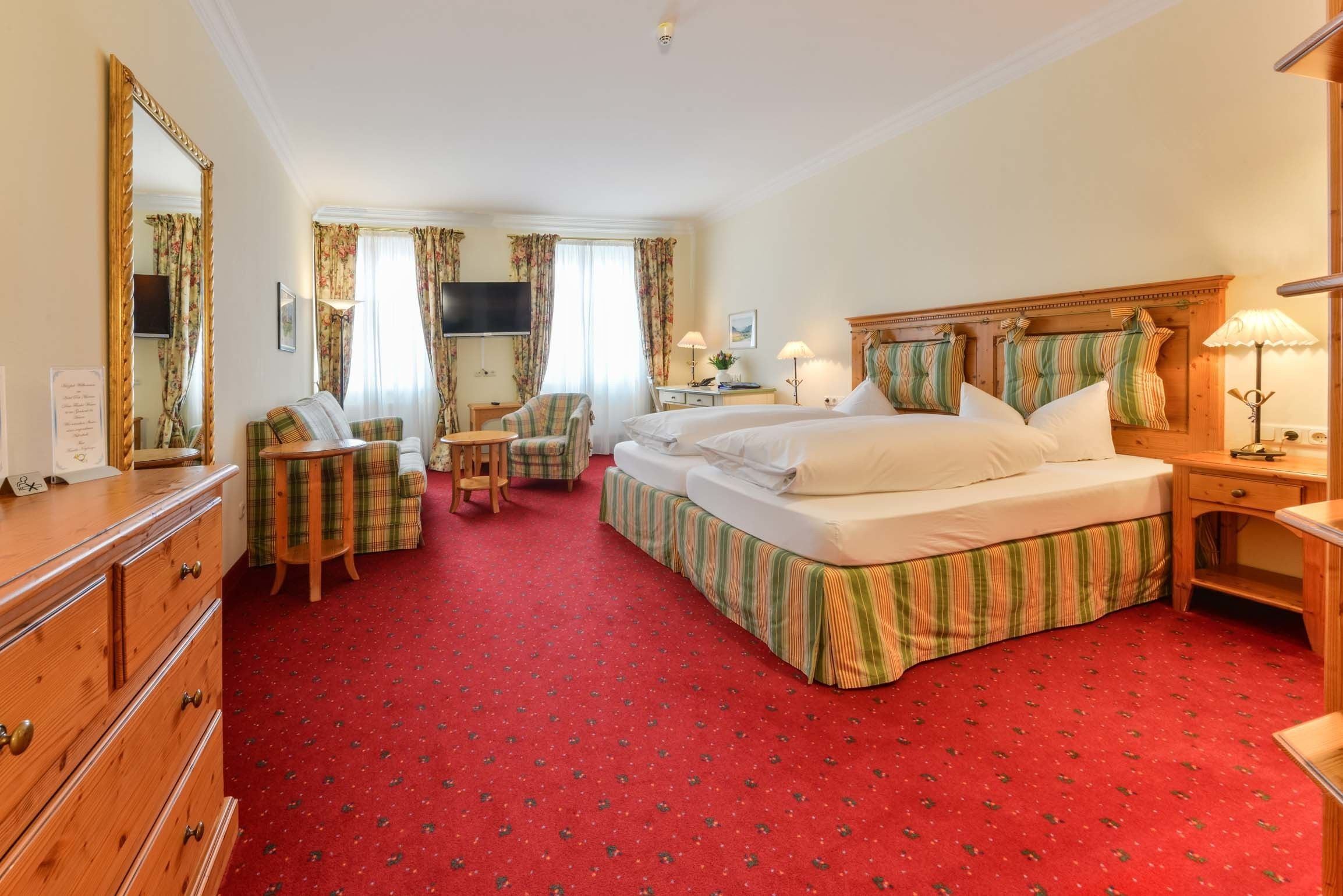 Una habitación de hotel con una cama grande, dos mesitas de noche, un aparador, una silla, una mesita pequeña y un televisor.