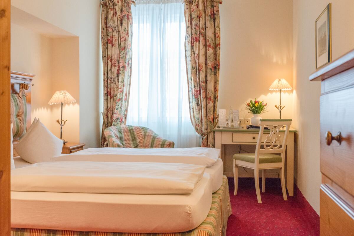 Habitación de hotel con cama, escritorio, silla, lámpara y ventana con cortinas.