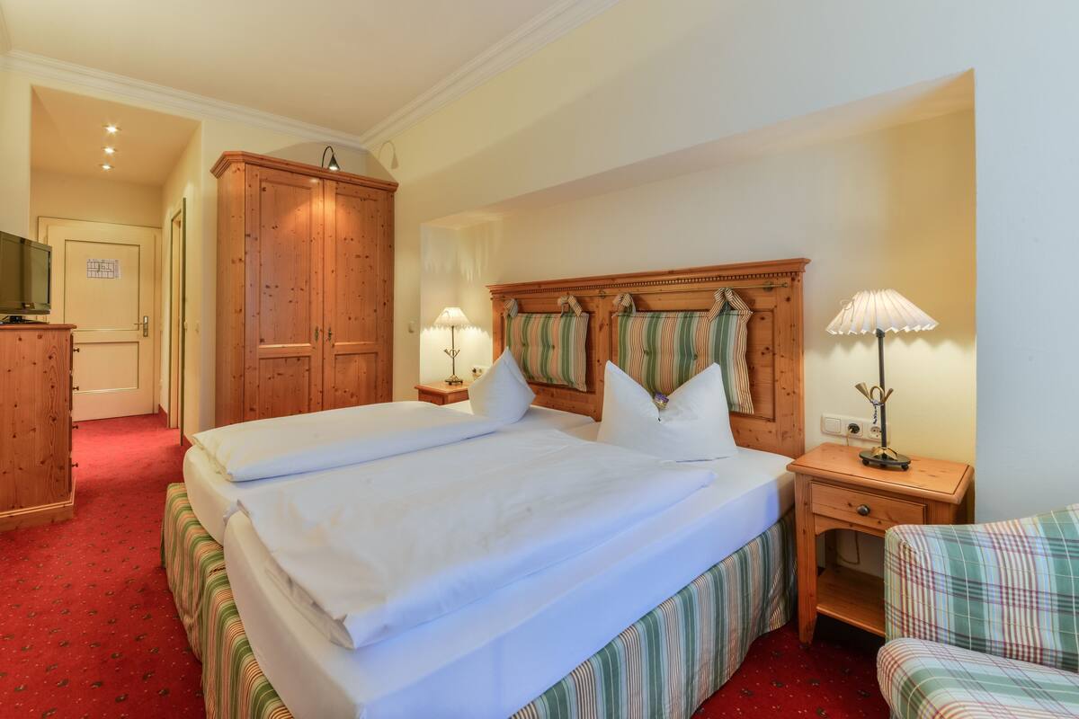Habitación de hotel con una cama grande, armario de madera, mesitas de noche y televisión.