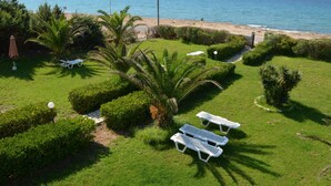 Un jardín cuidado con césped, palmeras y sillones de descanso blancos.