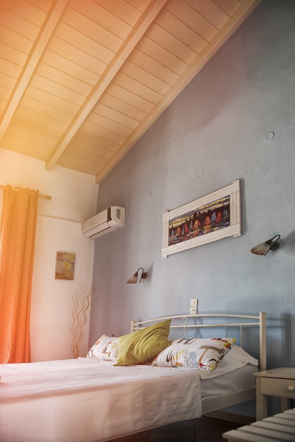 A bedroom with a bed, a painting on the wall, an air conditioning unit, and a nightstand.