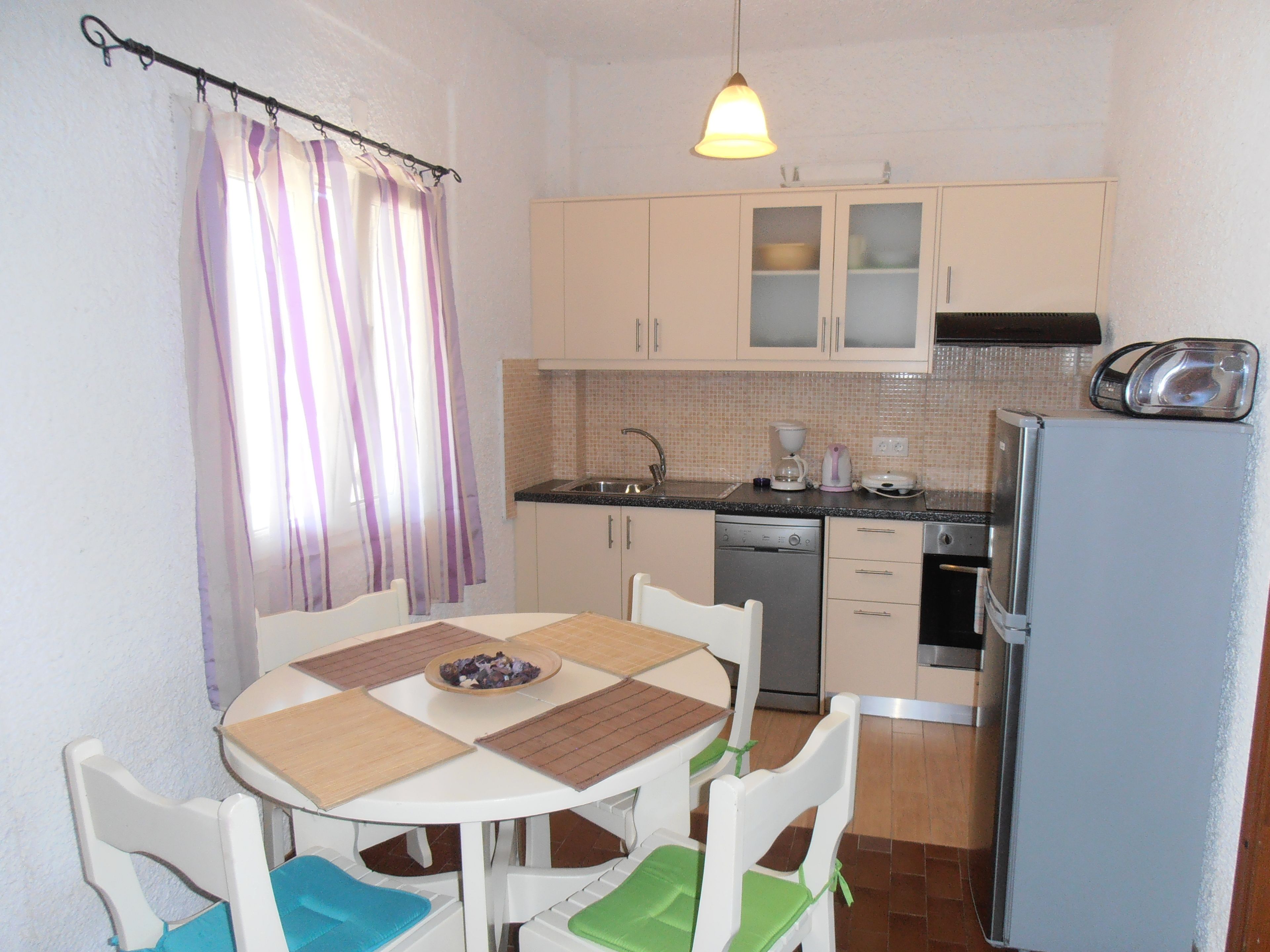 A compact kitchen with a dining table, chairs, a refrigerator, and a coffee maker.