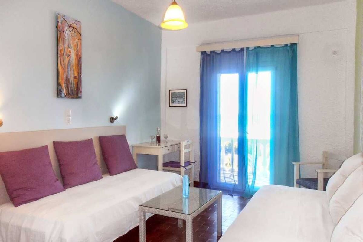 A hotel room with a bed, a small table, a chair, and a window with curtains.